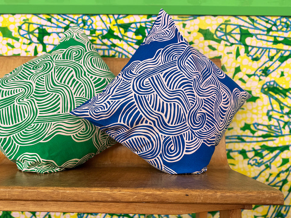 a green and a blue cushion both with white zen lines design sitting on a wodden bench