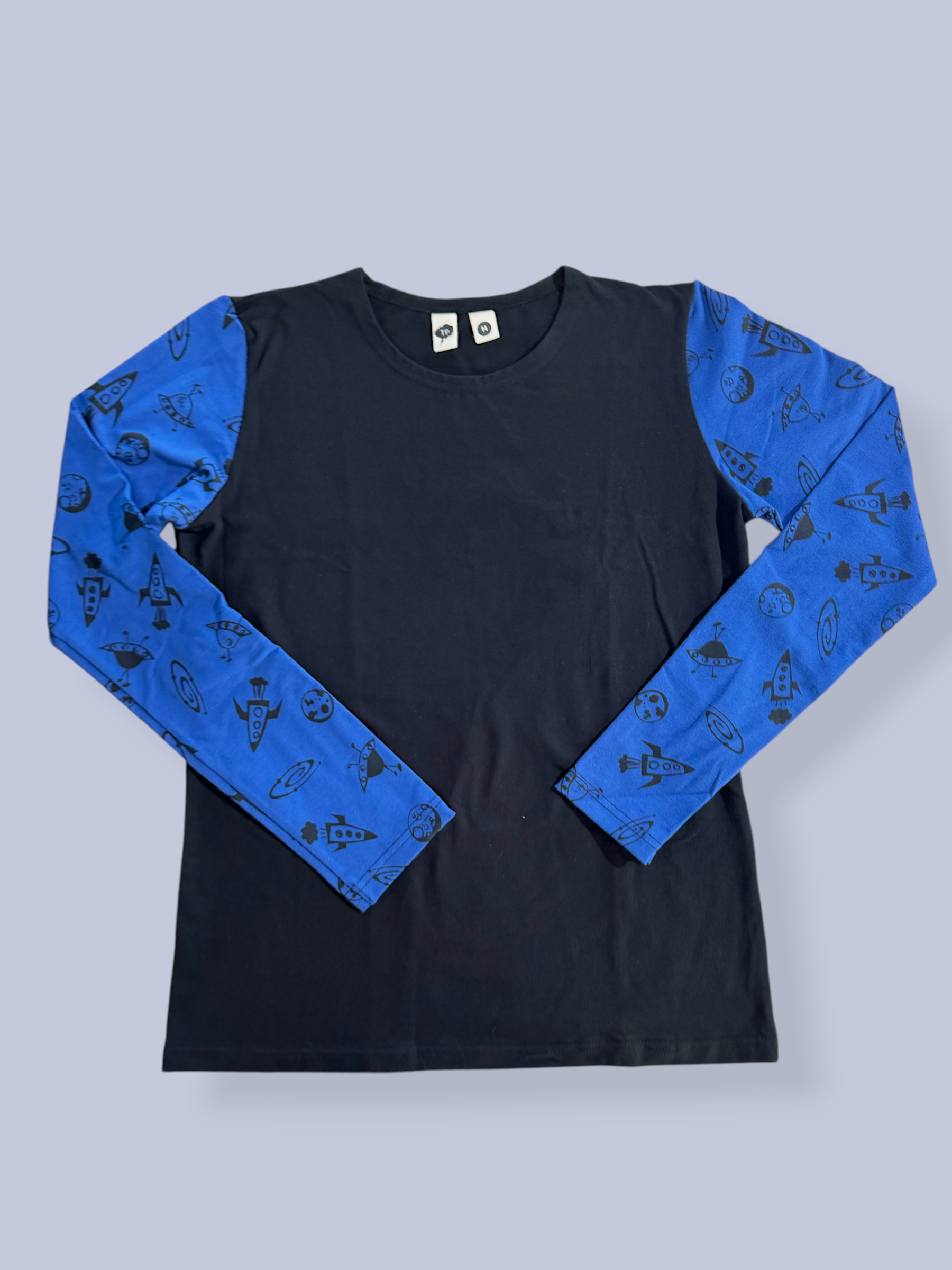 A long-sleeve t-shirt with a solid black body and bright blue sleeves featuring a black space-themed pattern of planets, stars, and rockets, laid flat against a light gray background.