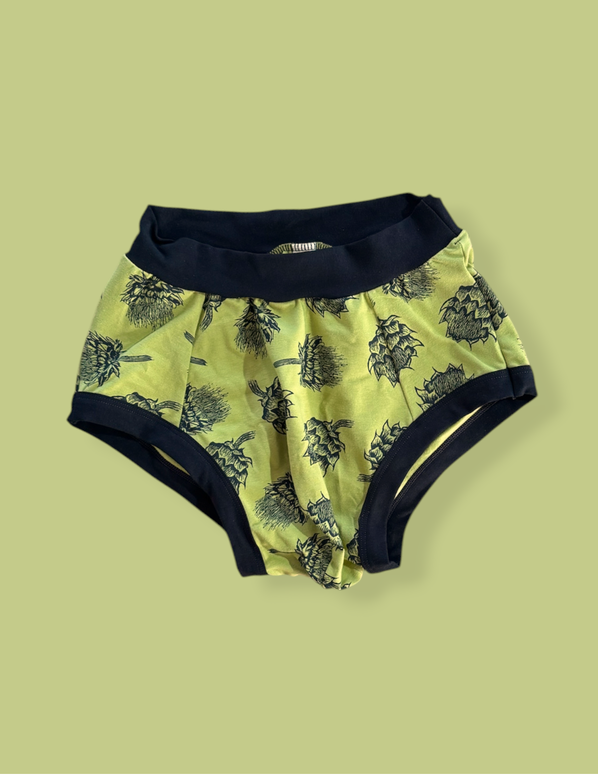 Yellow baby bloomers with black floral pattern on a light green background