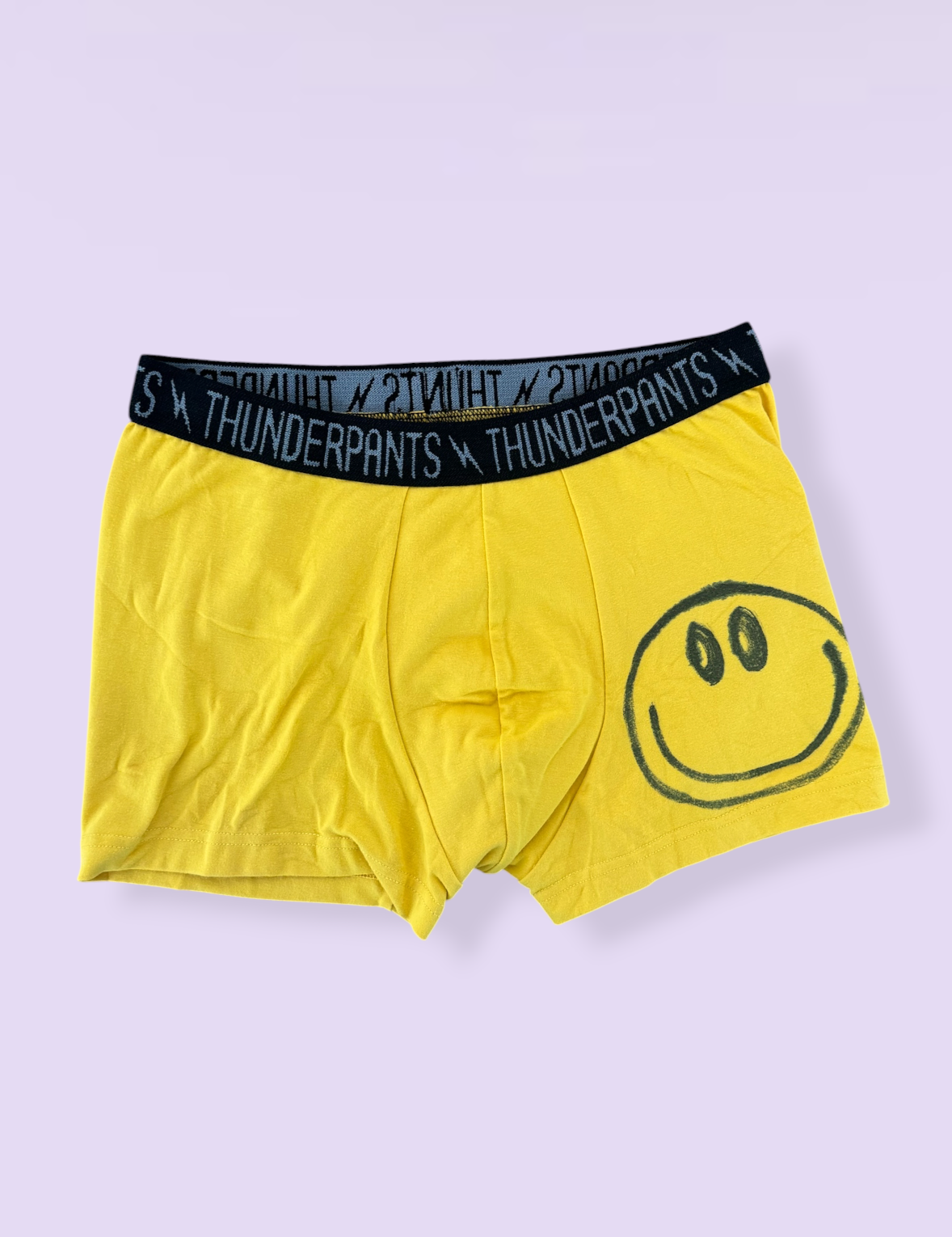 Yellow boxer briefs with a smiley face design and black waistband on a light purple background.