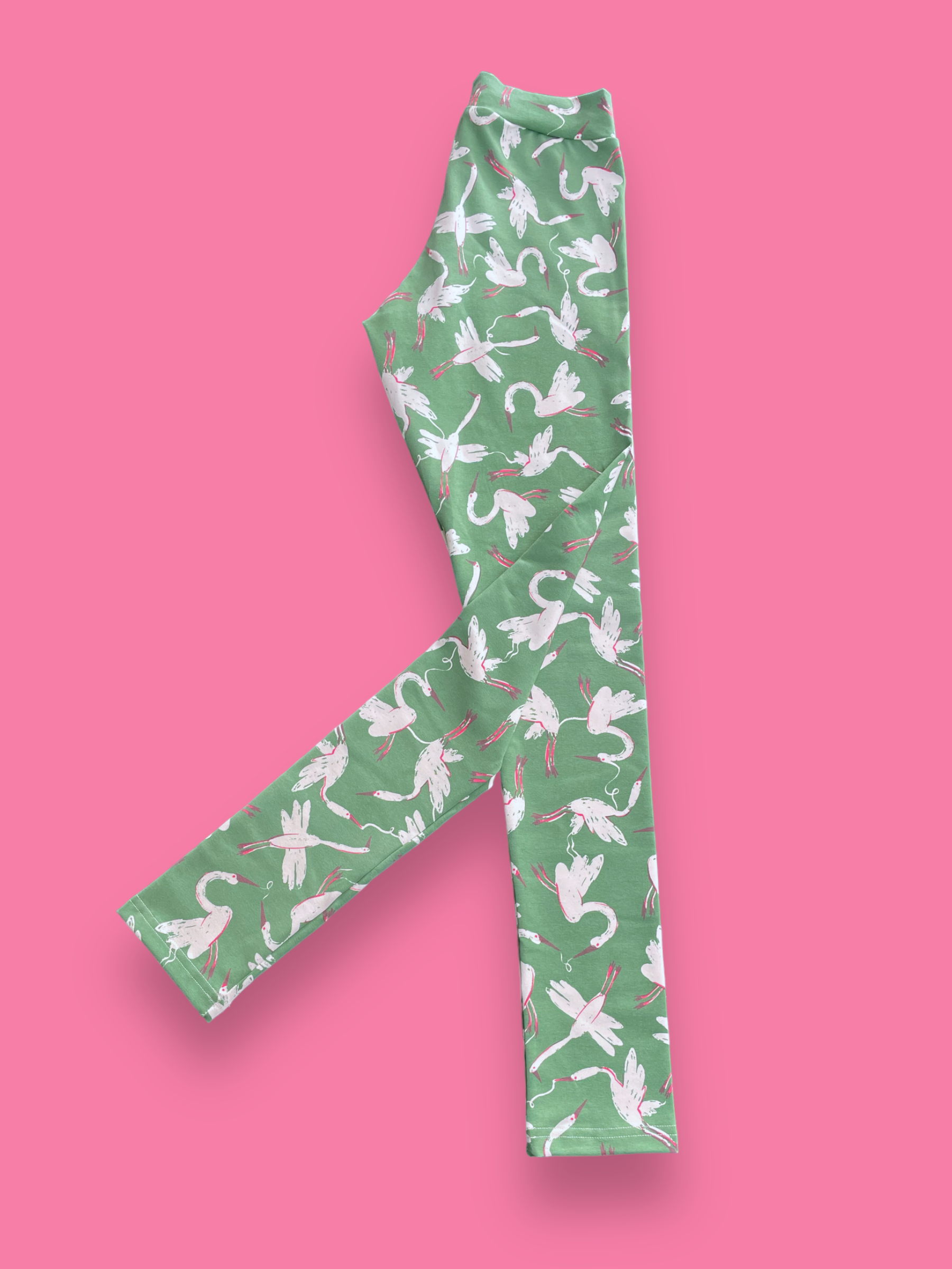 White swans with pink legs and a vintage green background printed on long adults tights layed flat.