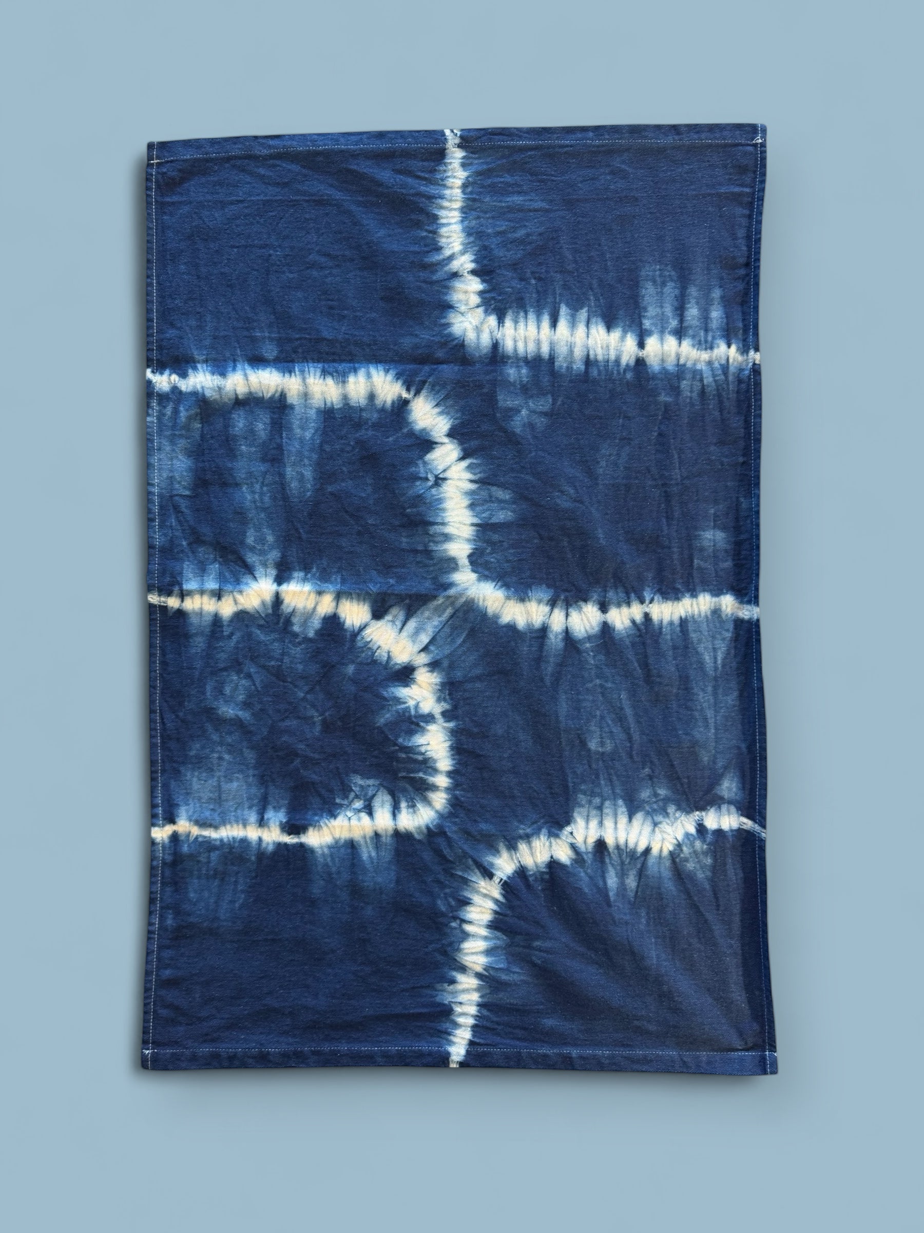 Tie-dye tea towel with blue and white pattern on a light blue background